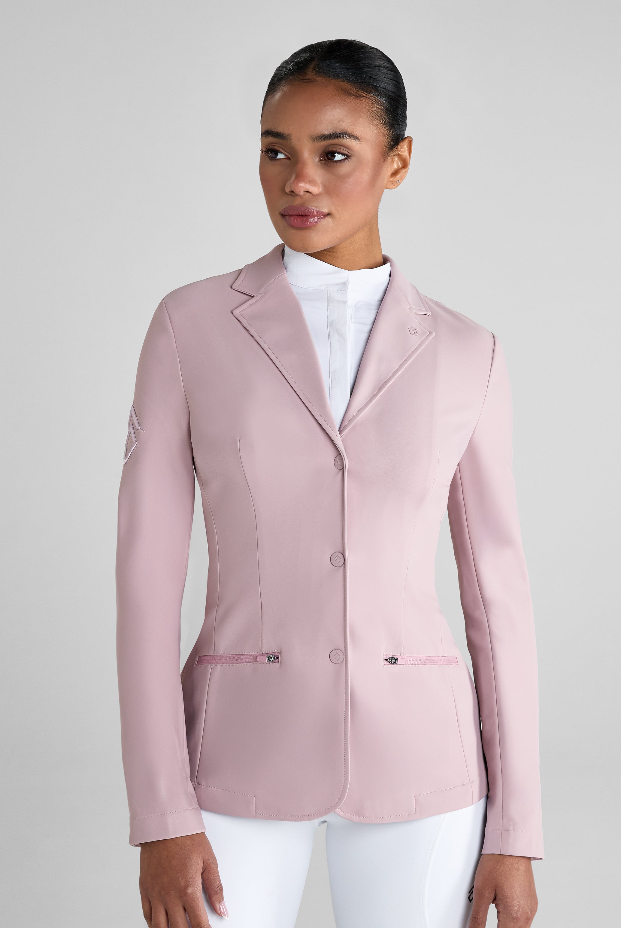 Woman wearing a light pink blazer over a white shirt and pants on a gray background