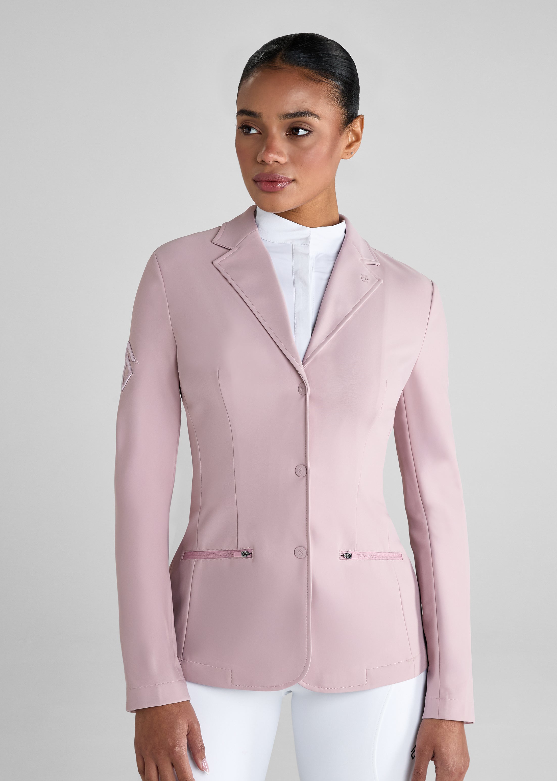 Woman wearing a light pink blazer over a white shirt and pants on a gray background
